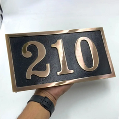 House number sign '210'—brass address plaques held by a person on a white background