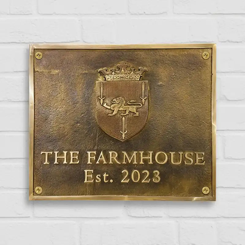 Custom Engraved Brass Address Plaques with crest and 'The Farmhouse Est. 2023' text on a white brick wall background