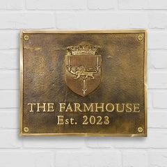 Custom Engraved Brass Address Plaques with crest and 'The Farmhouse Est. 2023' text on a white brick wall background