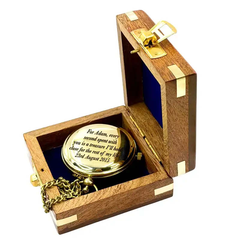Gold pocket watch in an open wooden box with engraved text on a white background