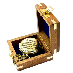 Gold pocket watch in an open wooden box with engraved text on a white background