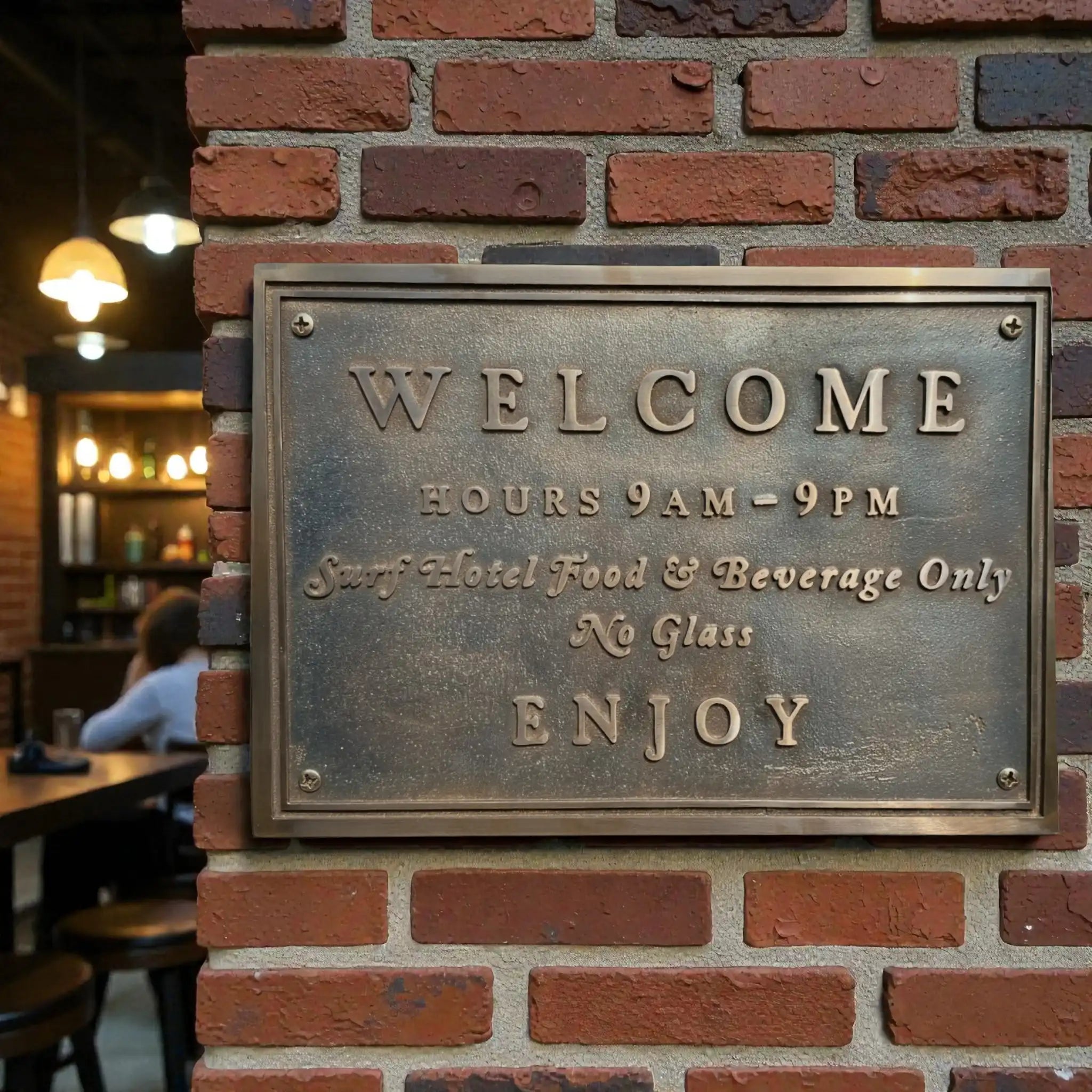 Metallic welcome sign on a brick wall with restaurant interior in the background