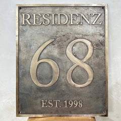 Historic-style bronze plaque with 'RESIDENZ 68 EST. 1998' text on a light gray background