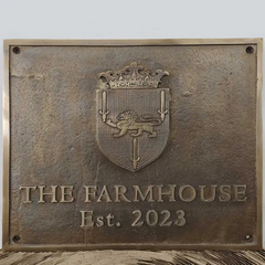 Bronze plaque with a crest and 'The Farmhouse Est. 2023' text on a wooden surface. Outdoor bronze address plaque