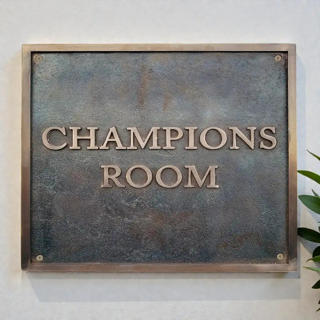 Bronze address plaque  with 'Champions Room' text on a white wall 