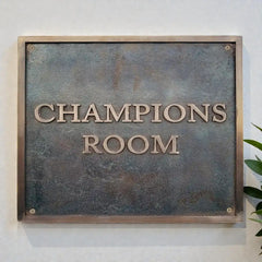 Bronze address plaque  with 'Champions Room' text on a white wall 