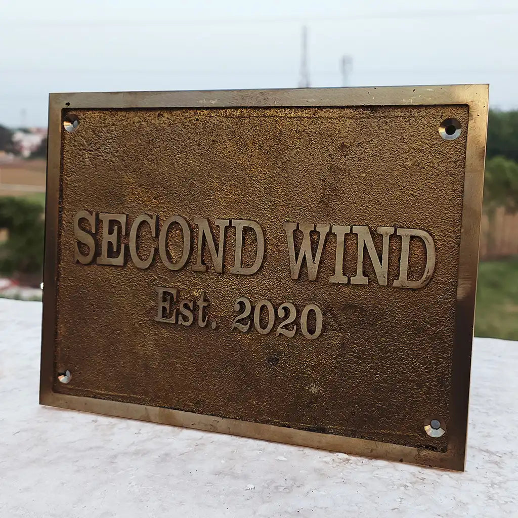 Bronze plaque with 'SECOND WIND Est. 2020' text on a blurred outdoor background