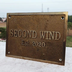Bronze plaque with 'SECOND WIND Est. 2020' text on a blurred outdoor background