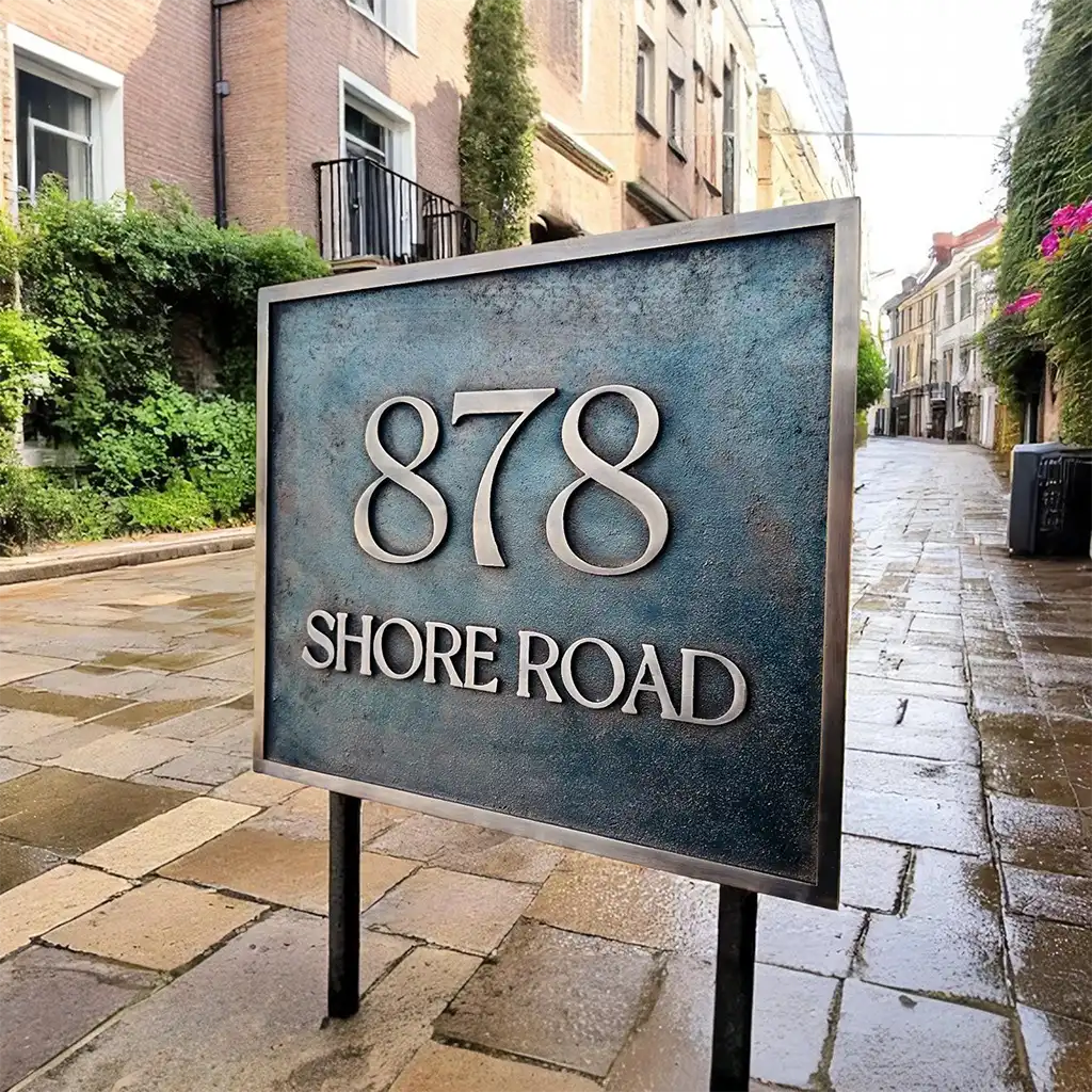 Bronze address sign for 878 Shore Road on a stone sidewalk with buildings in the background. bespoke bronze plaque