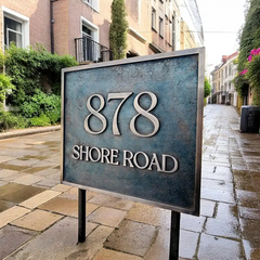 Bronze address sign for 878 Shore Road on a stone sidewalk with buildings in the background. bespoke bronze plaque