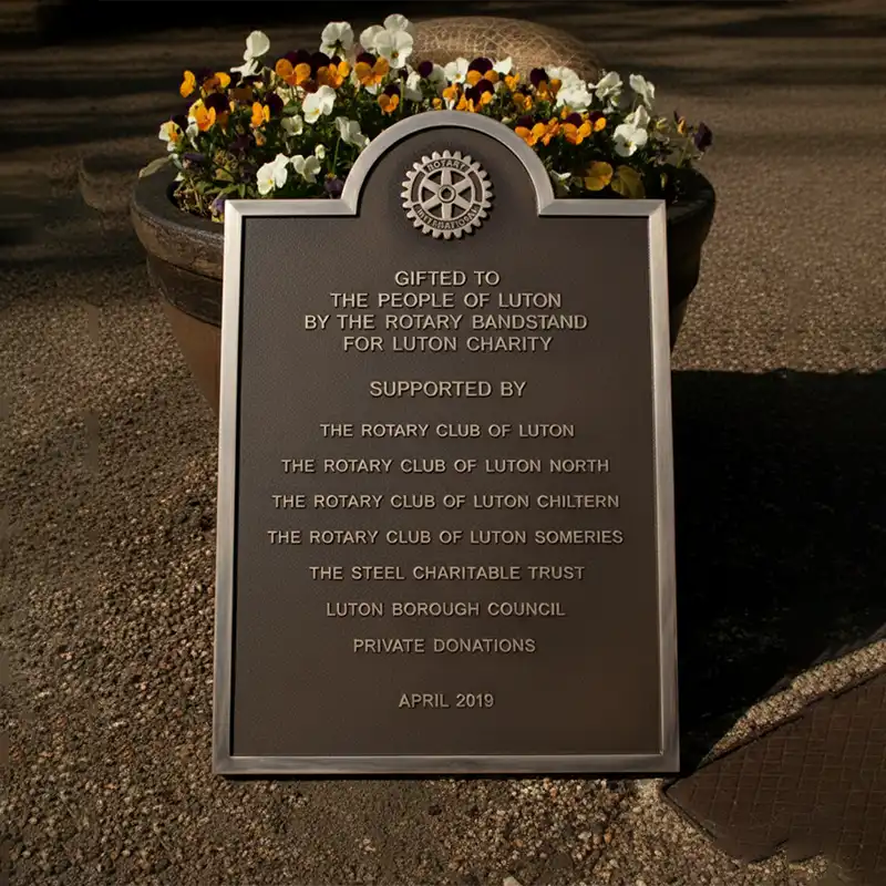 Plaque dedicated to Luton by the Rotary Bandstand for Luton Charity with flowers in the background.