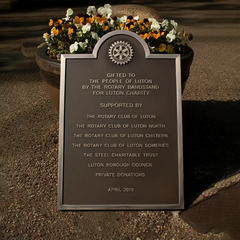 Plaque dedicated to Luton by the Rotary Bandstand for Luton Charity with flowers in the background.