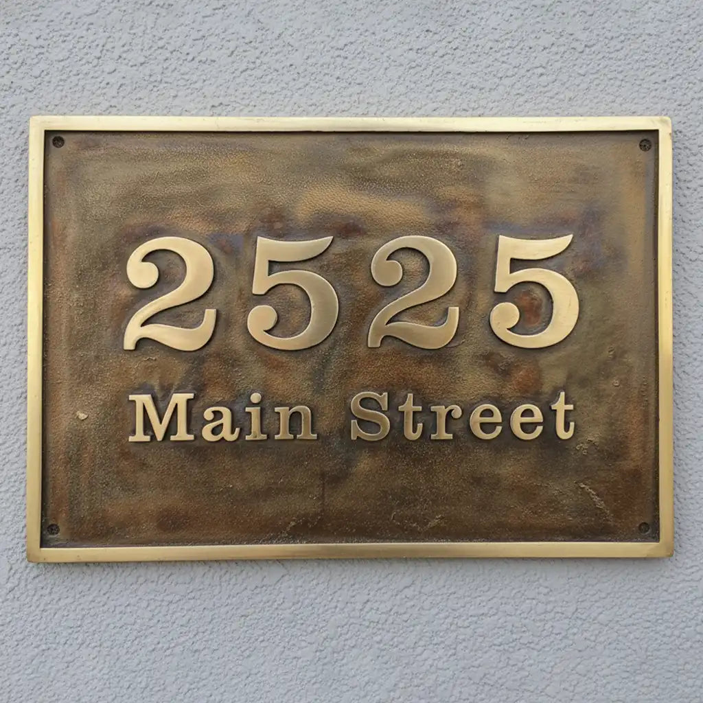 Bronze house number sign with custom text on a gray wall