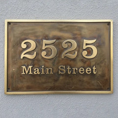 Bronze house number sign with custom text on a gray wall