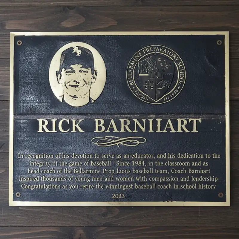 A bronze dedication plaque honoring Rick Barnhiart for his contributions to baseball education, displayed on a wooden surface.