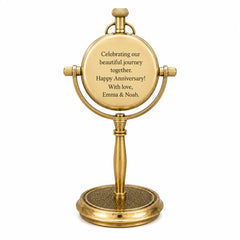 A gold-finished tabletop vanity mirror with a round engraved plaque on the front that reads, 'Celebrating our beautiful journey together. Happy Anniversary! With love, Emma & Noah.