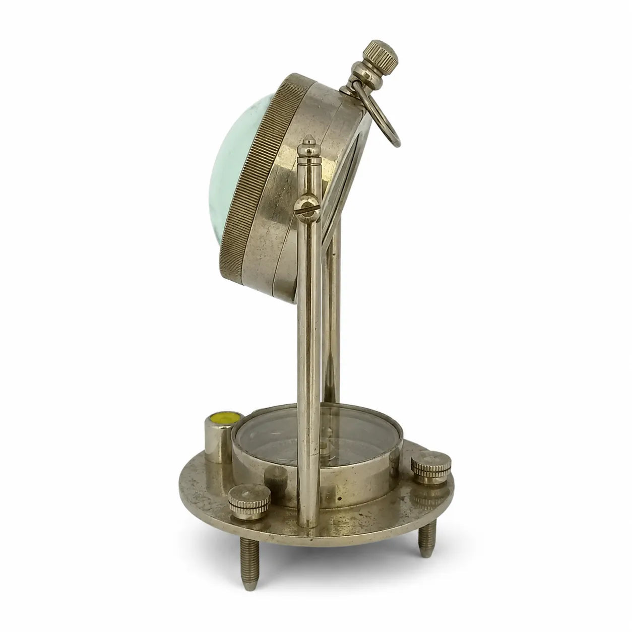 An antique brass surveyor's transit or level instrument with a circular base, adjustable vertical stand, and a tilted reading head over a green-tinted lens, shown on a white background.