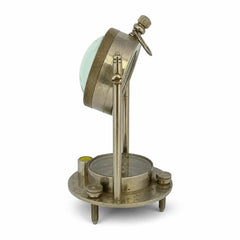 An antique brass surveyor's transit or level instrument with a circular base, adjustable vertical stand, and a tilted reading head over a green-tinted lens, shown on a white background.