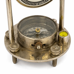 Close-up of a vintage-style metal transit or surveying instrument with a circular compass, adjustment knobs, threaded legs, and a small yellow level bubble on a white background.