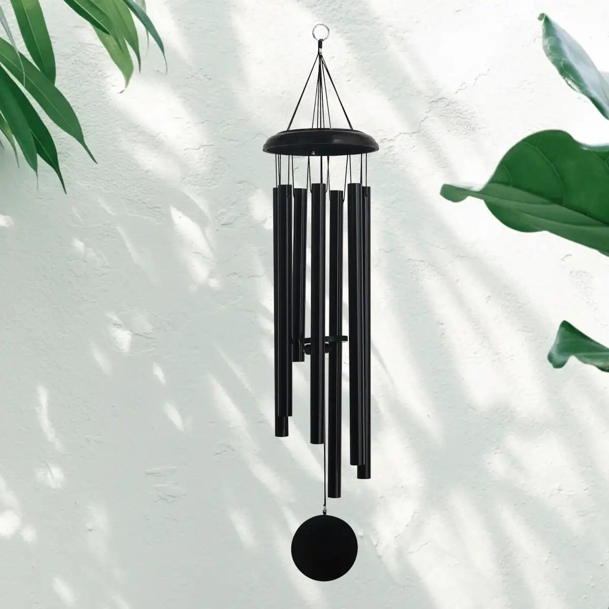 A black Corinthian bell wind chime hanging against a light background with green leaves
