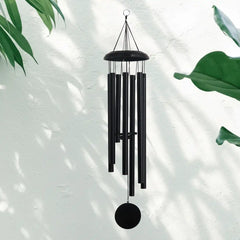 A black Corinthian bell wind chime hanging against a light background with green leaves
