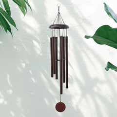 A brown Corinthian bell wind chime hanging against a light background with green leaves