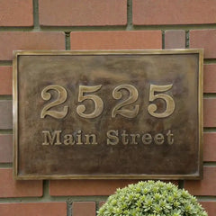 Bronze house number sign with '2525 Main Street' on a brick wall.