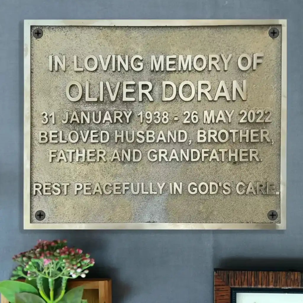 Memorial plaque for Oliver Doran on a gray wall with a plant in the corner.