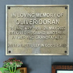 Memorial plaque for Oliver Doran on a gray wall with a plant in the corner.