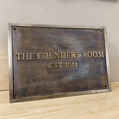 Bronze Metal plaque with 'The Founder's Room EST. 2011' text on a wooden surface.