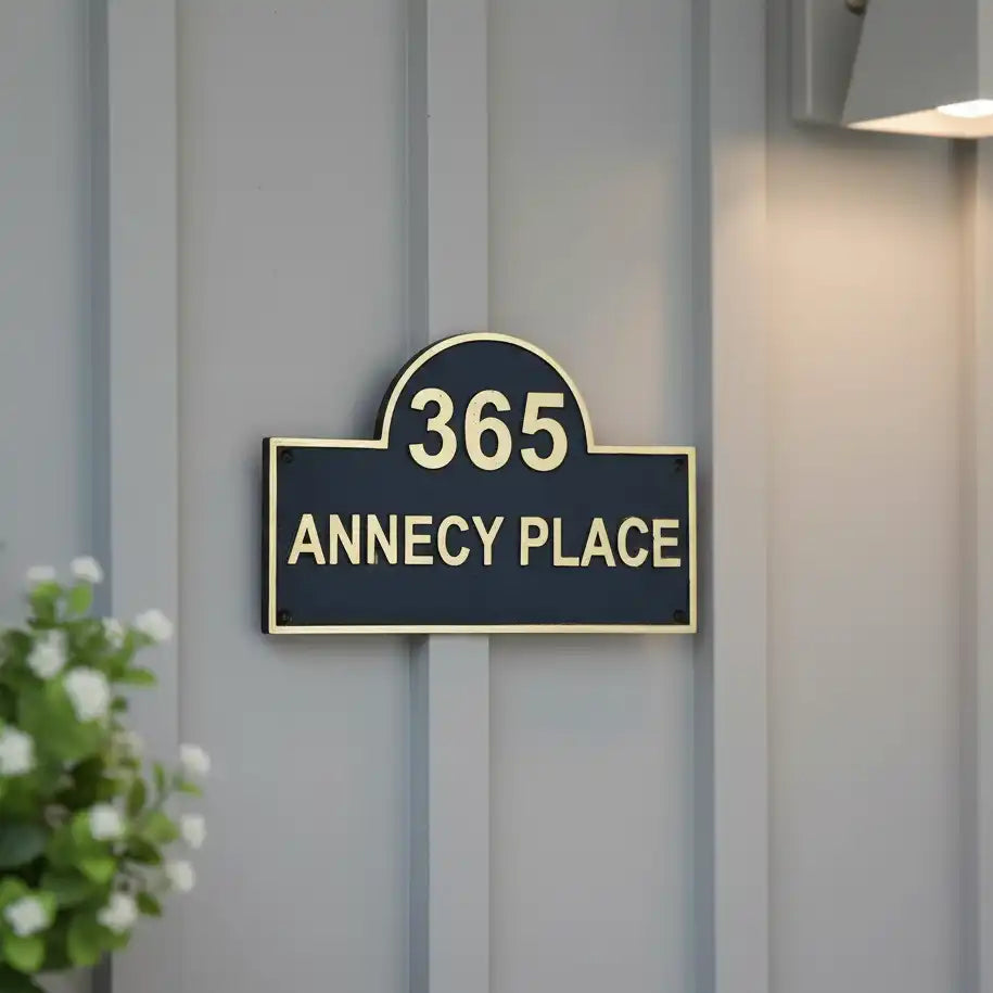 Stylish Black Finish Brass House Number Sign on a gray wall with a plant in the corner.