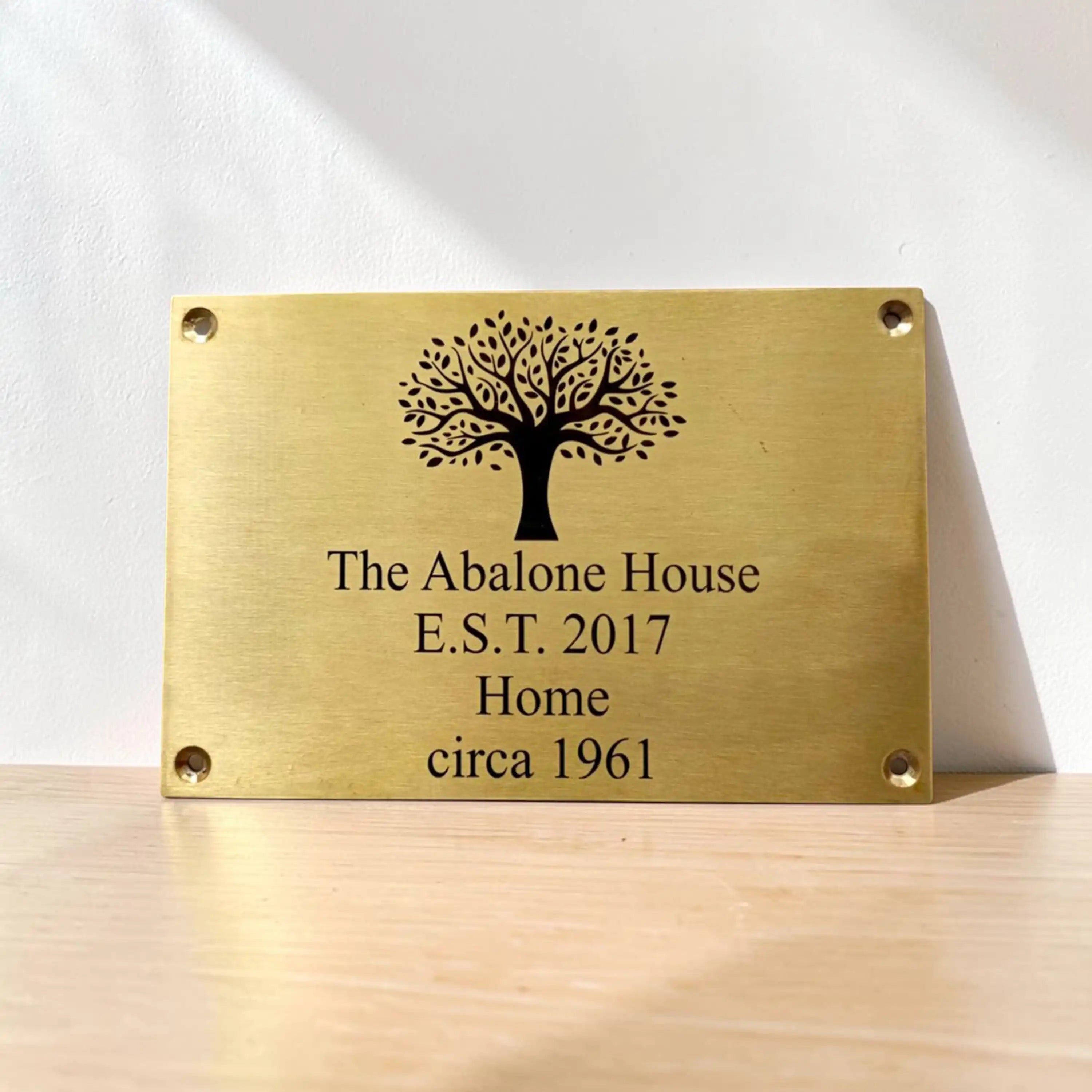 Brass plaque with tree design and engraved text on a wooden surface
