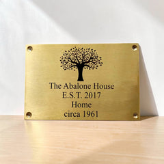 Brass plaque with tree design and engraved text on a wooden surface