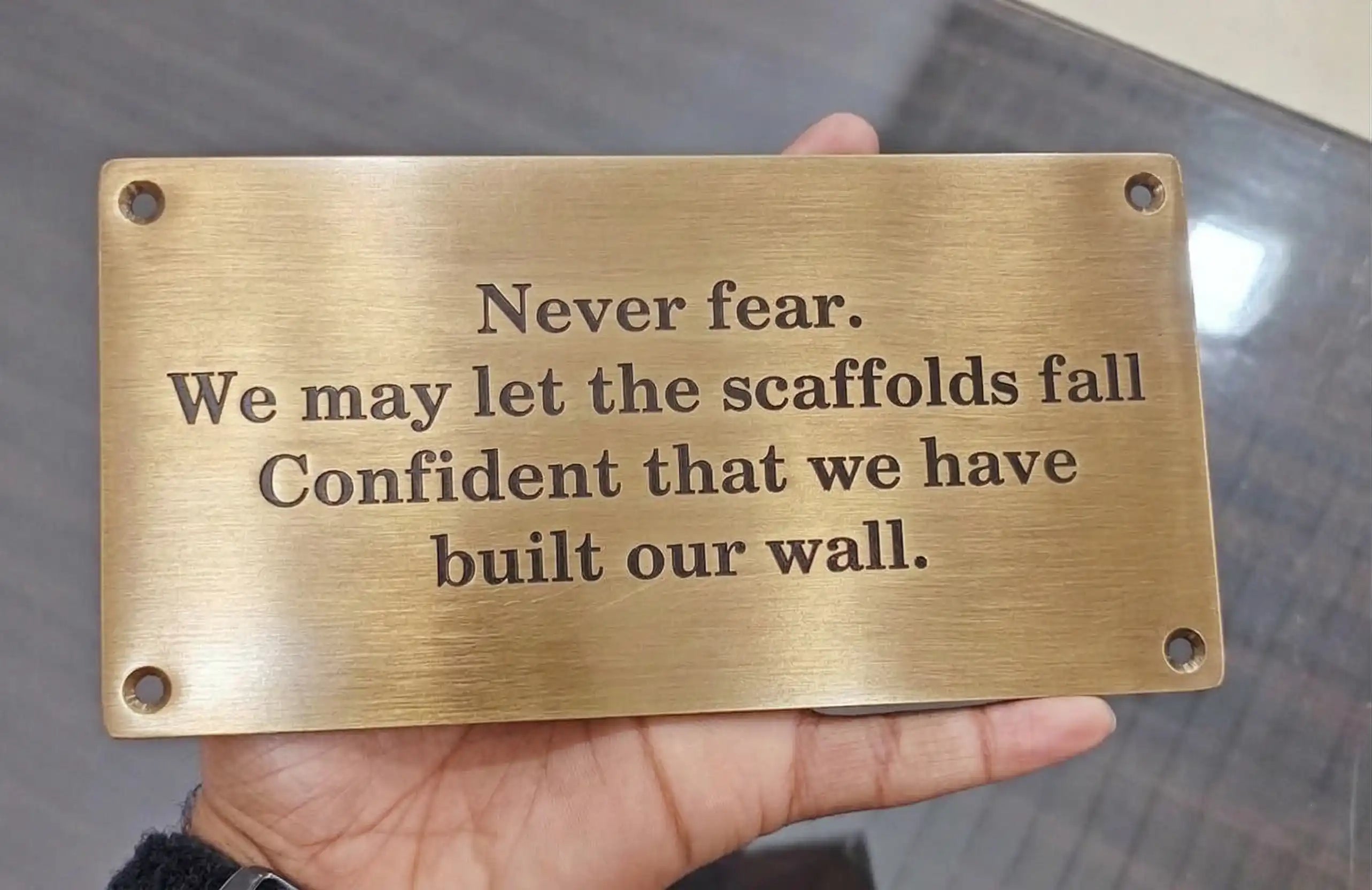 Brass plaque with engraved text held in a hand against a blurred background