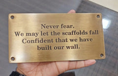 Brass plaque with engraved text held in a hand against a blurred background
