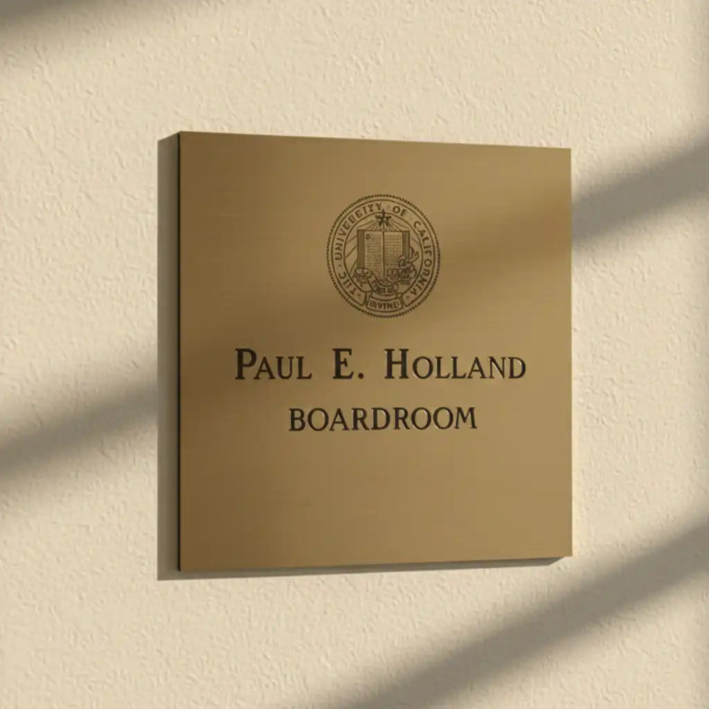 Brass plaque with personalized engraving with 'Paul E. Holland Boardroom' text and university emblem on a beige wall.