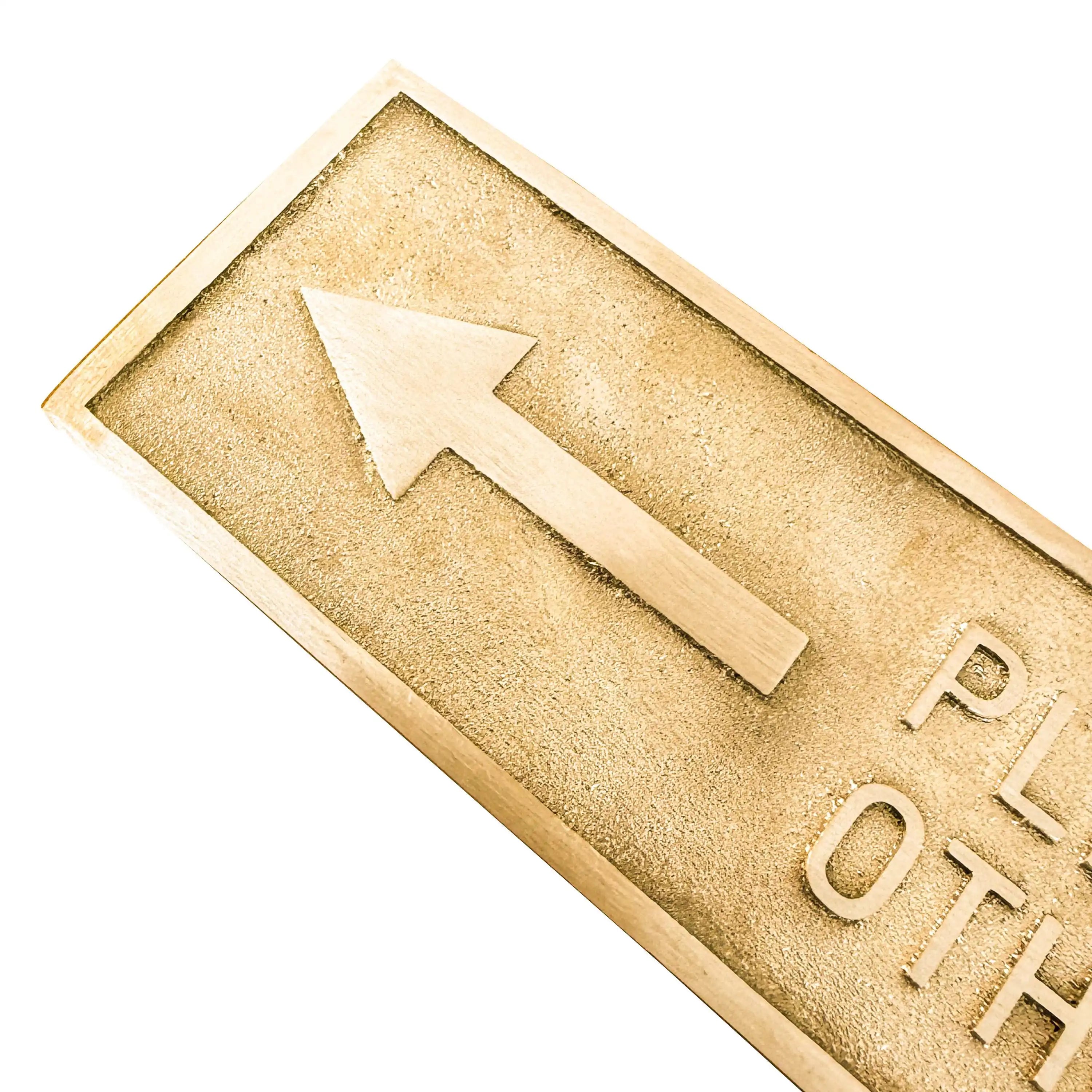 Gold-colored rectangular brass door sign with an arrow and text on a white background