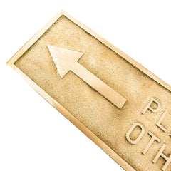 Gold-colored rectangular brass door sign with an arrow and text on a white background