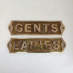 Two brass signs labeled 'GENTS' and 'LADIES' on a white background