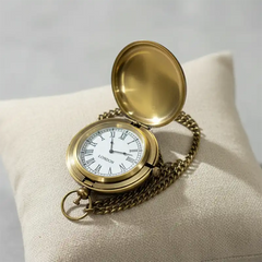 Vintage gold brass pocket watch on a beige cushion with a light gray background