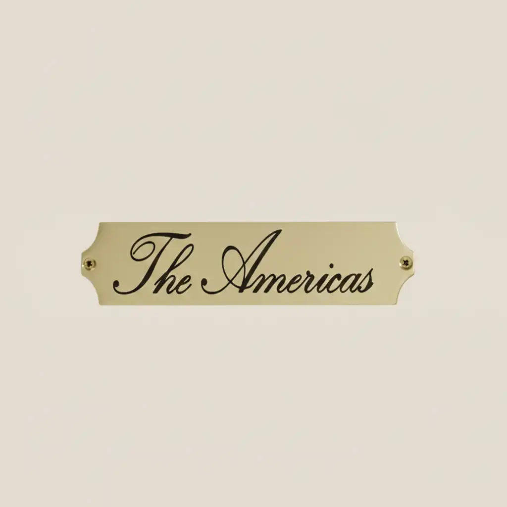 Engraved Brass Plate for Office Door—Gold plaque with 'The Americas' text on a beige background