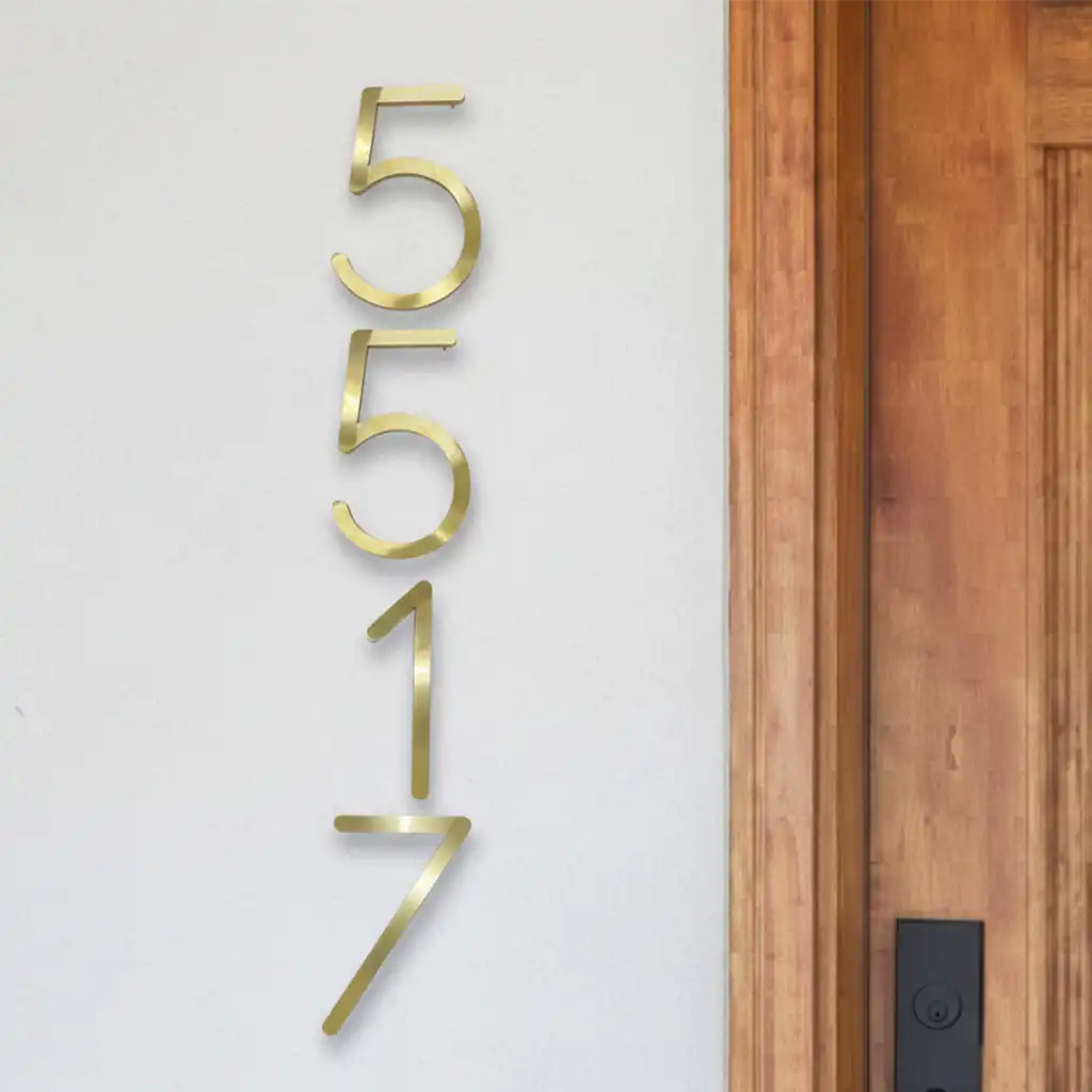 Engraved brass home address plate on a white wall next to a wooden door.