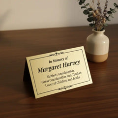 Personalized brass memorial plate on a wooden surface with a vase of flowers.
