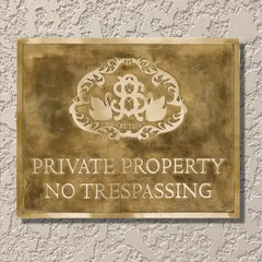 Brass plaque with decorative design and 'Private Property No Trespassing' text on a textured wall.