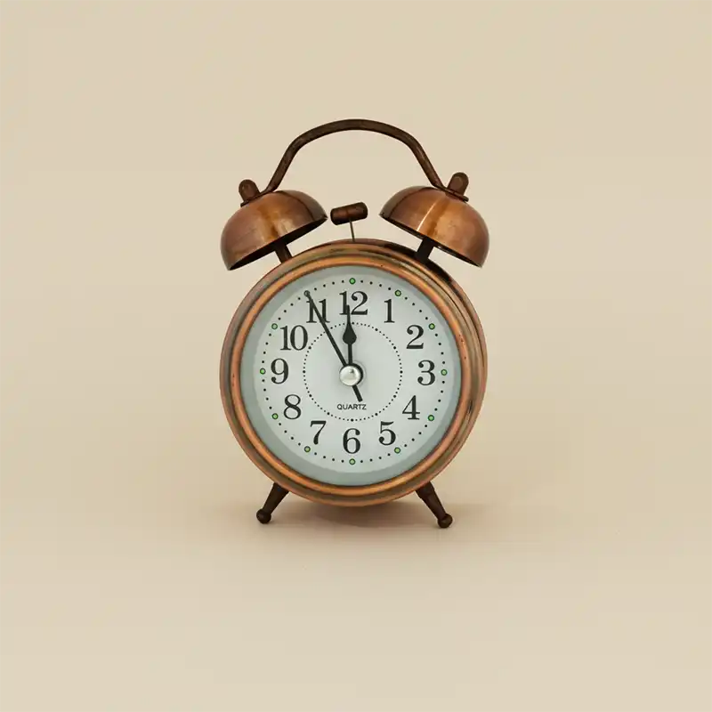 Vintage-style alarm clock with brass finish on a beige background