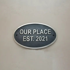 Oval metal sign with 'OUR PLACE EST. 2021' text on a beige background
