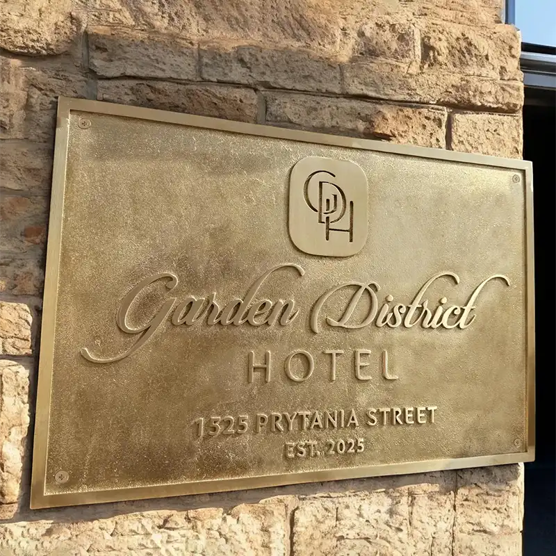 Brass plaque on a stone wall for the Garden District Hotel with contact information.