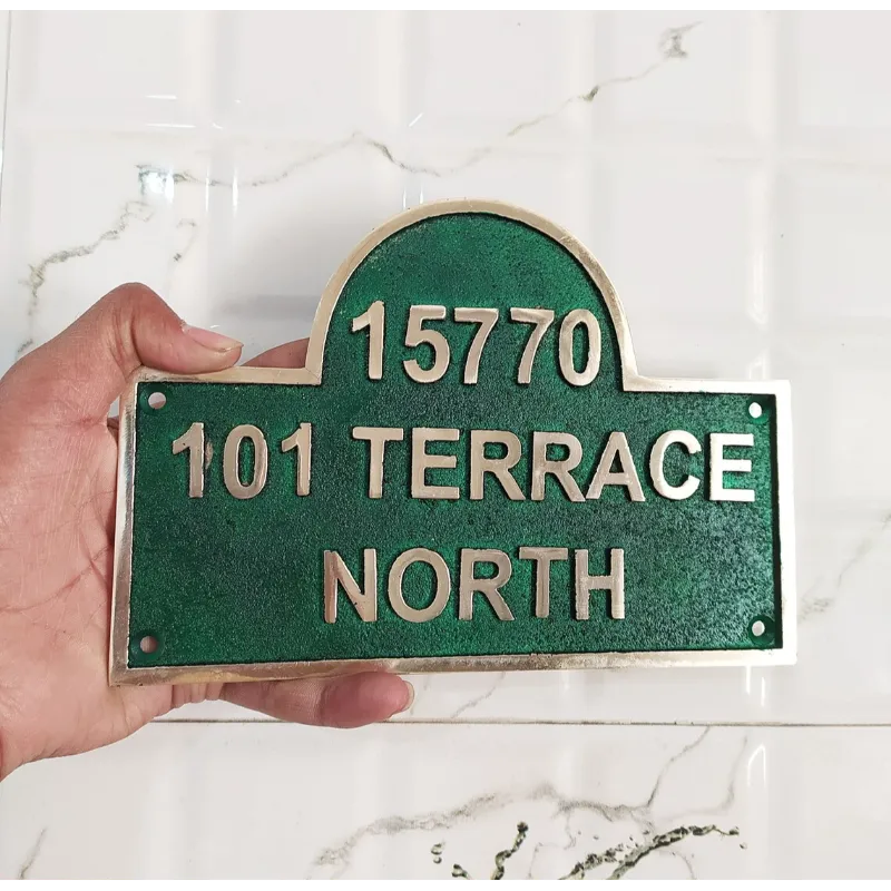 A custom address brass plaque plate with green text on a white background, held by a hand, displaying an example of personalized addressing.