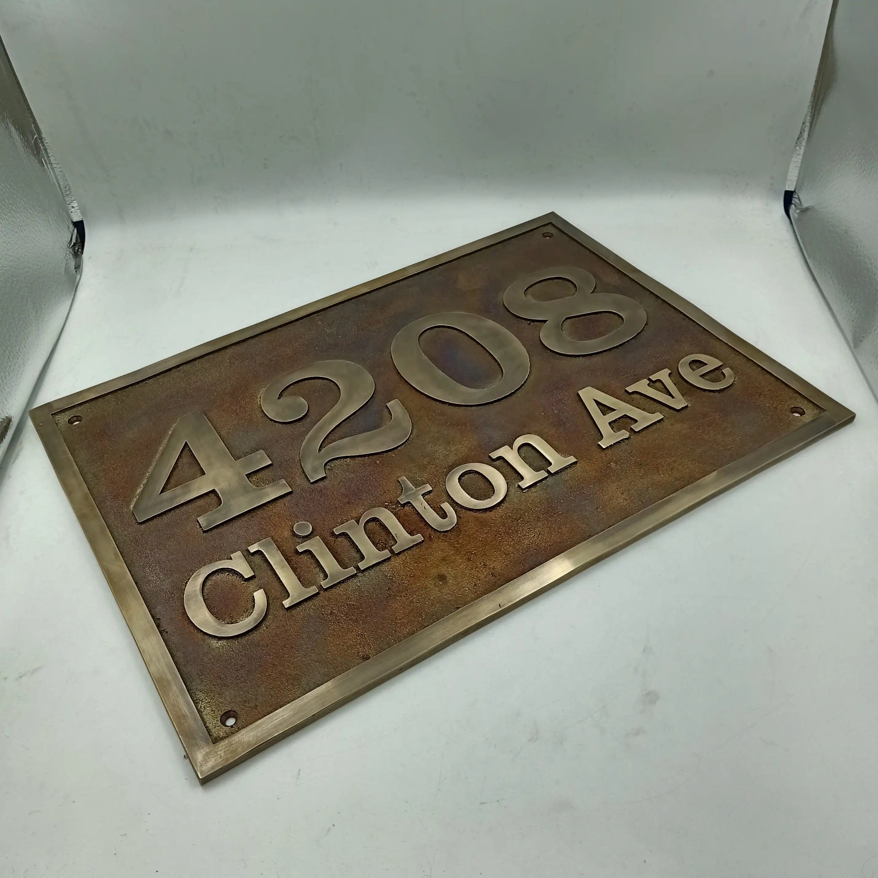 Rust-colored brass house number sign with '4208 Clinton Ave' on a white background