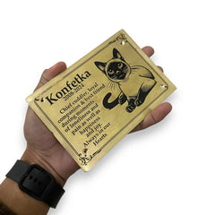 Hand holding a Brass plaque with a cat illustration and text on a white background